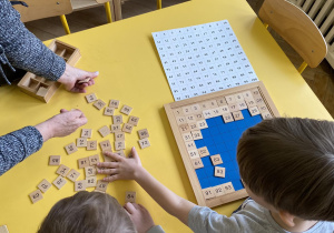 Zdjęcie przedstawia kobietę z dziećmi przy tablicy do 100.