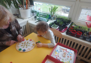 Zdjęcie przedstawia kobietę i dziewczynkę, układające klocki na palecie.