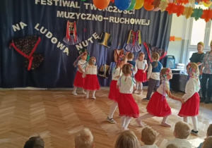 Zdjęcie przedstawia dzieci ubrane w stroje biało- czerwone. Dzieci prezentują taniec ludowy.