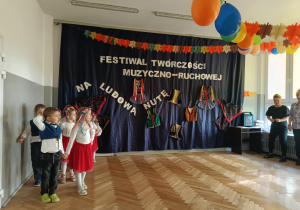 Zdjęcie przedstawia dzieci ustawione parami jedno za drugim. Na drugim planie znajduje się dekoracja.