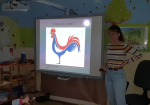 Zdjęcie przedstawia wolontariuszkę przy tablicy multimedialnej, podczas gdy prowadziła prelekcję o swoim kraju.
