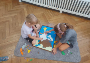 Zdjęcie przedstawia dwie dziewczynku układające na dywaniku mapę Europy.