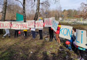 Dzieci trzymające transparent z haslem "Duzi czy mali w pomaganiu doskonali".