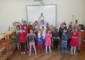 Zdjęcie przedstawia dzieci ustawione do zdjęcia. Dzieci mają w górze ręce, w których trzymają czekolady.