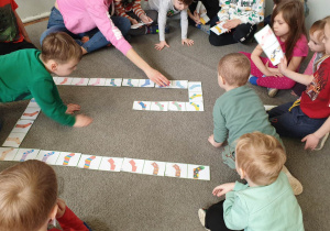 Zdjęcie przedstawia dzieci siedzące na dywanie. Dzieci układają domino ze skarpetek.