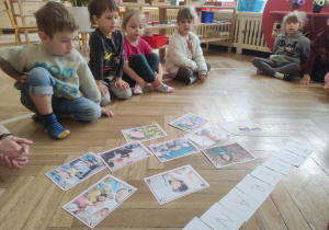 Zdjęcie przedstawia dzieci siedzące w na podłodze. Przed nimi leżą zdjęcia przedstawiające różne dzieci.