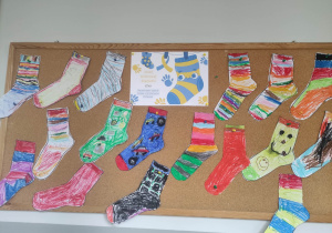 Zdjęcie przedstawia tablicę korkową na której zostały przyczepione kolorowe skarpety z papieru wykonane przez dzieci.