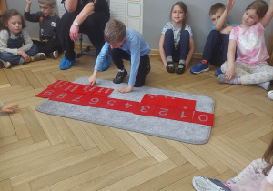 Zdjęcie przedstawia chłopca układającego liczby na dywaniku.