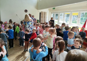 Zdjęcie przedstawia dzieci i nauczycieli biorących udział w zabawie tanecznej. Dzieci tańcząc trzymają się za ramiona.