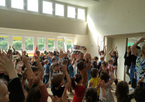 Zdjęcie przedstawia dzieci biorące udział w zabawie muzyczno- ruchowej. Dzieci podnoszą ręce w górze.