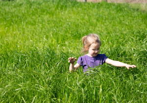 Zdjecie przedstawia dziewczynkę biegającą w wysokiej trawie