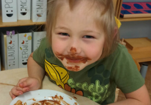 Zdjęcie przedstawia dziecko kończące jeść owoce w czekoladzie. Dziecko ma twarz w czekoladzie.