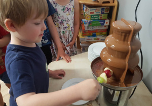Zdjęcie przedstawia chłopca korzystającego z fontanny z czekoladą.