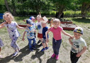 Zdjęcie przedstawia dzieci tańczące w ogrodzie.
