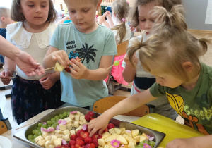 Zdjęcie przedstawia dzieci robiące szaszłyki z owoców.