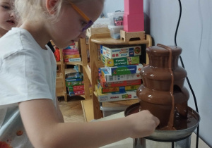 Zdjęcie przedstawia dziewczynkę korzystającą z fontanny z czekolady.