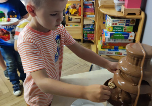Zdjęcie przedstawia chłopca korzystającego z fontanny z czekolady.