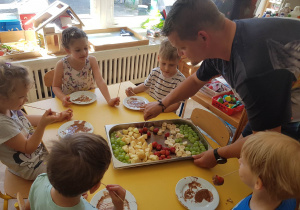 Zdjęcie przedstawia dzieci jedzące owoce z czekoladą.