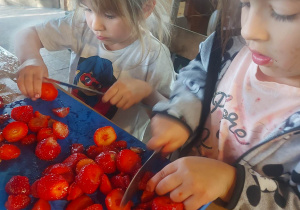 Zdjęcie przedstawia dziewczynki, które kroją truskawki potrzebne do gofrów, które dzieci przygotowywały według receptury