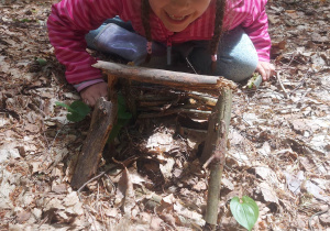 Zdjęcie przedstawia dziewczynkę, która z patyków konstruuje most