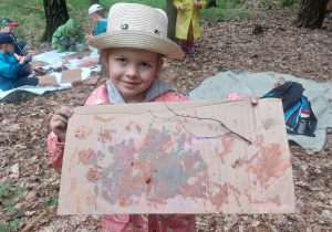 Zdęcie przedstawia dziewczynkę prezentują swój obraz malowany farbami pozyskanymi z gliny