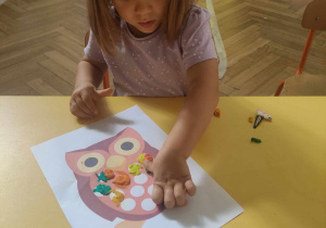 Zdjęcie przedstawia dziewczynkę, która wykleja plasteliną sowę.