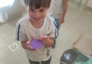 Zdjęcie przedstawia chłopca, który znajduje się w łazience a w rękach trzyma fioletową kropkę.