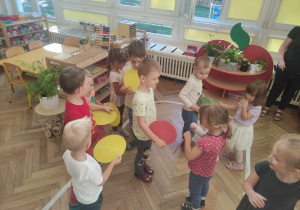 Zdjęcie przedstawia dzieci biorące udział w zabawie muzyczno- ruchowej. Dzieci trzymają w dłoniach kolorowe kropki.