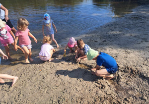 Zdjęcie przedstawia grupę dzieci, która z piasku buduje kanał