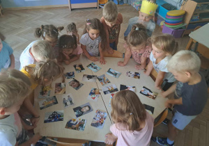 Zdjęcie przedstawia dzieci stojące wokół stołu i oglądające zdjęcia.