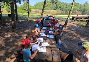Zdjęcie przedstawia dzieci siedzące przy stole i robiące prace plastyczne.