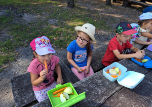 Zdjęcie przedstawia dzieci jedzące marchewki i jabłka.