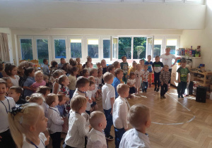Zdjęcie przedstawia dzieci z całego przedszkola i nauczycieli biorących udział w zabawie muzycznej z pokazywaniem.