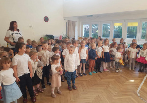 Zdjęcie przedstawia dzieci z całego przedszkola i nauczycieli śpiewających hymn przedszkolaka.