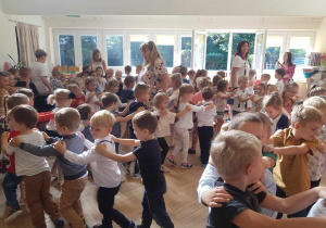 Zdjęcie przedstawia dzieci i nauczycieli biorących udział w zabawie muzyczno- ruchowej.