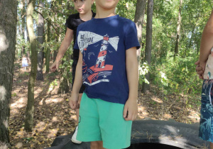 Zdjęcie przedstawia chłopca stojącego na dużej oponie w lesie.