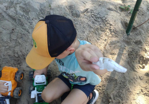 Zdjęcie przedstawia chłopca szukającego w piaskownicy dinozaurów.
