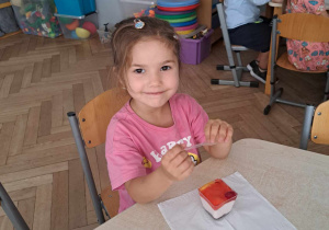 Zdjęcie przedstawia dziewczynkę siedzącą przy stole, na którym stoi ciastko.