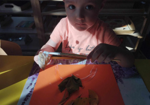 Na zdjęciu widzimy chłopca, który przykleja liście na papier.