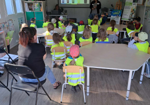 Zdjęcie przedstawia dzieci siedzące na krzesłach i oglądające prezentację.