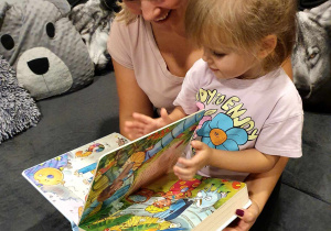 Zdjęcie przedstawia kobietę, czytającą dziewczynce książkę.