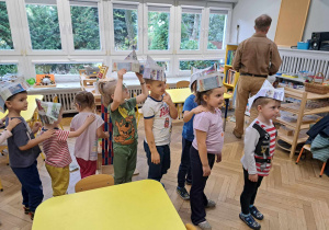 Zdjęcie przedstawia dzieci stojące jedno za drugim, w papierowych czapkach na głowie.
