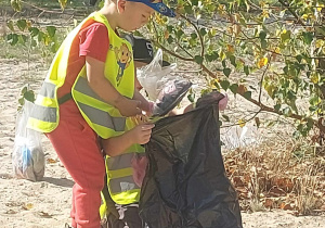 Zdjęcie przedstawia małego chłopca, który wrzuca zebrane śmieci do worka