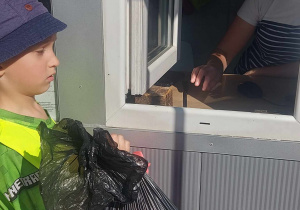 Zdjęcie przedstawia chłopca, który przekazuje zebrane przez dzieci śmieci pracownikowi sortowni