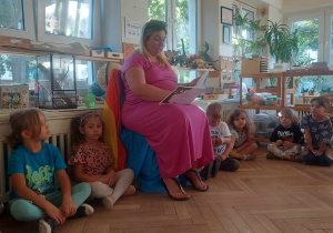 Na zdjęciu widać mamę Mikołaja podczas głośnego czytania. Wokół mamy siedzą zebrane w kole dzieci