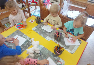 Na zdjęciu widać dzieci siedzące przy stoliku i rysujące to co usłyszały podczas czytania