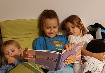 Zdjęcie przedstawia chłopca, który czyta swojemu młodszemu rodzeństwu