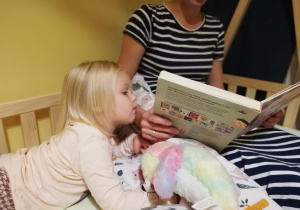 Zdjęcie przedstawia kobietę z dziewczynką podczas wieczornego czytania
