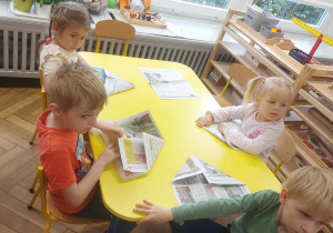 Na zdjęciu widać dzieci przy stoliku, które słuchają jak wykonać zadanie