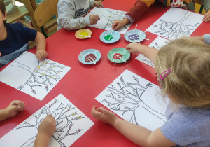 Dzieci malując patyczkami do uszu wykonują pracę plastyczną "Jesienne drzewo"